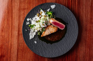 Ahşap bir masada soslu ızgara ton balığı bifteği.