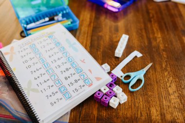 Matematik defterini makas ve okul malzemeleriyle ahşap masaya koy.