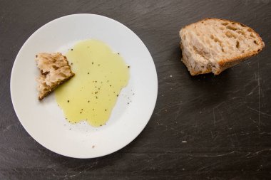 Beyaz bir tabakta duran bir parça ekmek ve parlak sarı zeytinyağı.