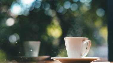 Kahve fincanı ahşap masada ve yeşil bokeh arkaplanda güneş doğarken..