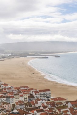 Beyaz evleri ve turuncu kiremitli çatıları olan caddelerin en üst görüntüsü, okyanus üzerinde antik bir Portekiz şehri. Nazare, Portekiz