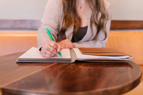 White woman sitting at brown circle table writing in notebook