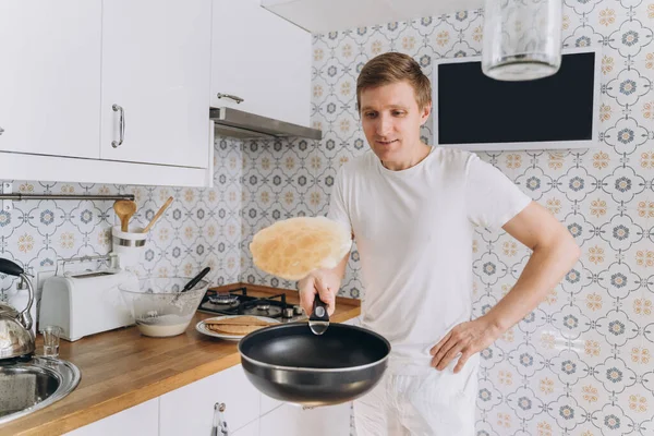 Man in white bake pancakes and toss them in a frying pan