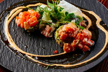 Sos soslu somon tartar ve siyah tabakta otlar.