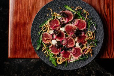 Siyah tabakta soslu mermer sığır eti carpaccio.