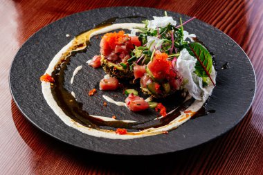 Sos soslu somon tartar ve siyah tabakta otlar.