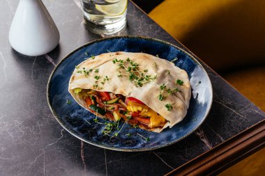 Tabağında et, sebze ve sos olan Türk pidesi.