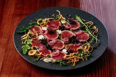 Siyah tabakta soslu mermer sığır eti carpaccio.