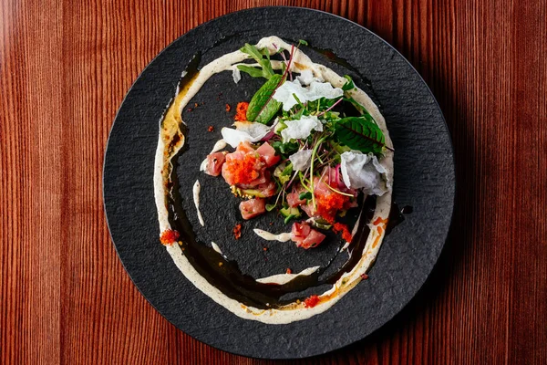 stock image salmon tartare with sauce and herbs on a black plate