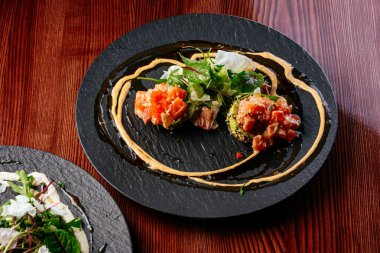 Sos soslu somon tartar ve siyah tabakta otlar.