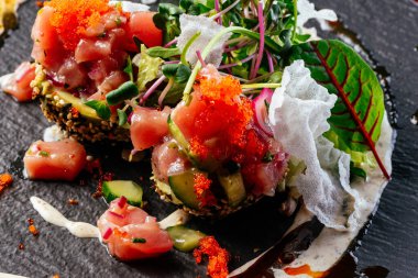 Sos soslu somon tartar ve siyah tabakta otlar.