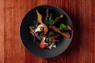 Soslu biftek ve siyah tabakta otlar.