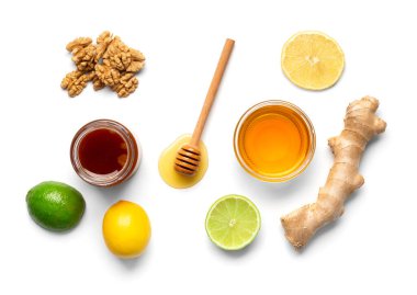 Composition of jars with honey, nuts, lemon, lime and ginger on isolation. Honey in bowls, dipper and fruits on a white background. Healthy breakfast foods.
