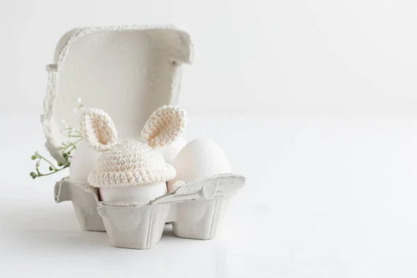 白い背景の卵箱にウサギの耳とかぎ針編みの帽子のイースターエッグ 横のバナー コピースペース付きのポストカード — ストック写真