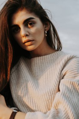 Kahverengi saçlı, beyaz kazaklı, iri gözlü kız.