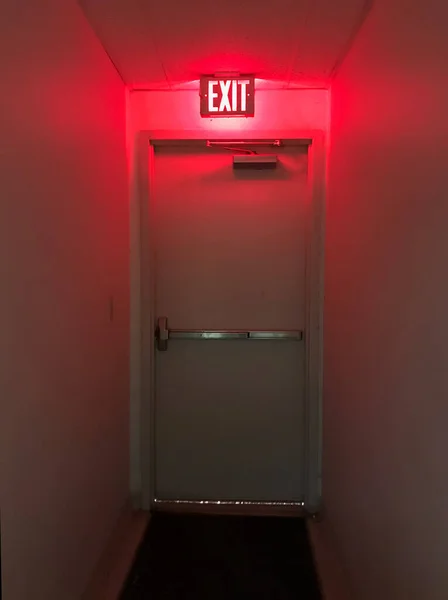 Emergency exit door at the end of the hall with the exit light on.
