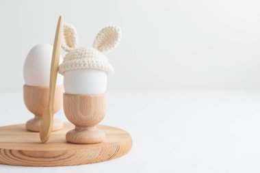 Örgü şapkalı paskalya yumurtası, beyaz arka planda tahta yumurta tutacağı olan tavşan kulaklı. Yatay pankart, kopyalanmış kartpostal