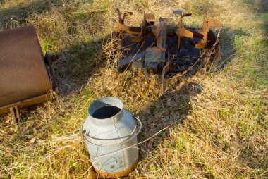 Paslı tarım ekipmanları ve süt kovası çimenlerde oturuyor..