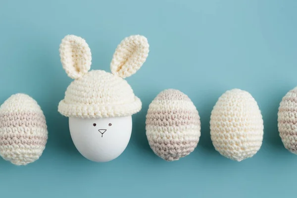 Easter egg in crochet hat with bunny ears on blue background. Flat lay. Horizontal banner, post card