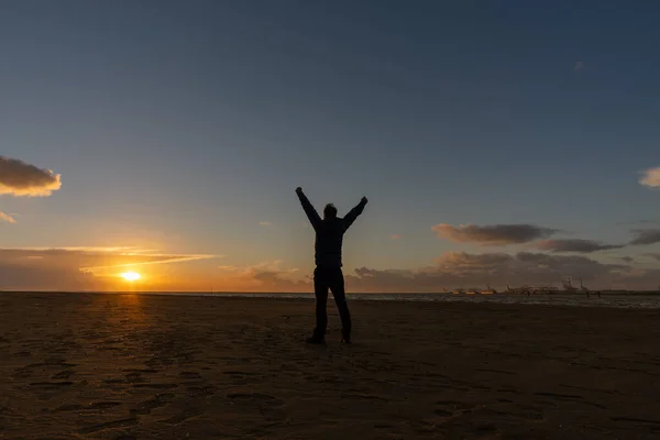 年轻人站在那里 举起胳膊 看着海滩上的落日 — 图库照片