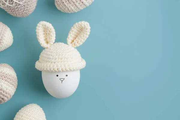 Easter egg in crochet hat with bunny ears on blue background. Flat lay. Horizontal banner, post card