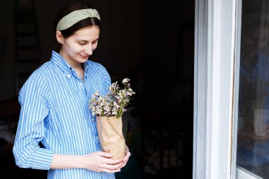 Mavi gömlekli kadın elinde çiçek paketini tutuyor.