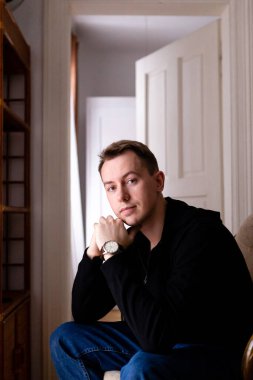 Siyah kazaklı ve kot pantolonlu sarışın bir adam dairesinde yalnızdı.