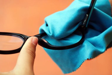 Mavi gözlüklerini mavi bir bezle temizleyen güzel genç kız.