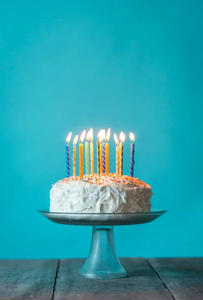 stock image Birthday cake with white icing and candles against blue background.