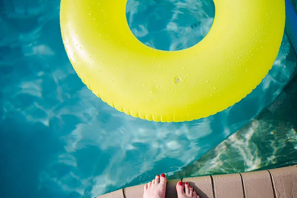 yellow inner tube in pool and women feet