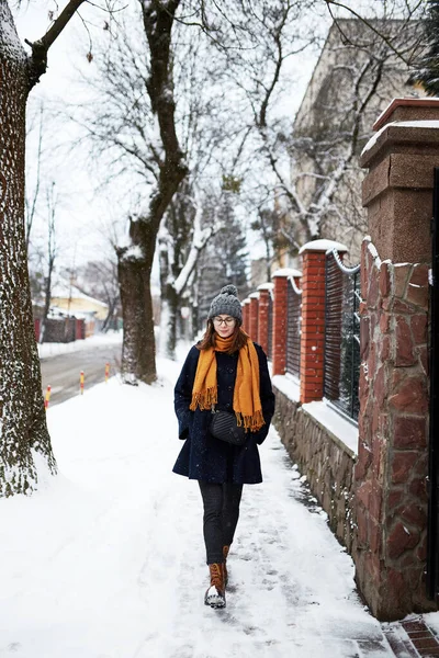 穿着黄色围巾和蓝色外套的女人独自走在雪地的街上 — 图库照片
