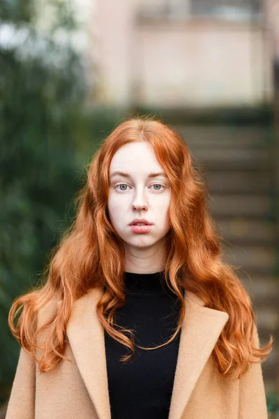コート姿の赤髪の女性が秋の晴れた公園を歩く — ストック写真