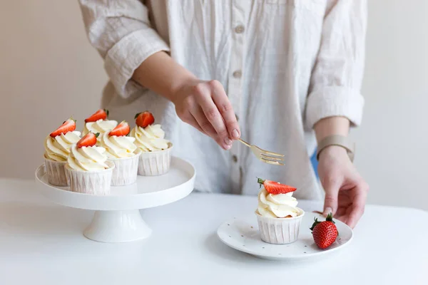 young woman cook tastes cream cupcake with fresh strawberries
