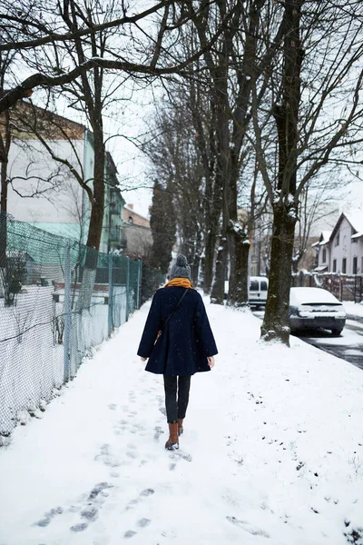 穿着黄色围巾和蓝色外套的女人独自走在雪地的街上 — 图库照片