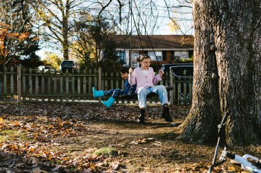 Kid cousins play on tree swing in fall in front yard neighborhood clipart