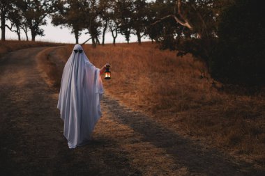 Person dressed in a ghost Halloween costume holding a lantern clipart