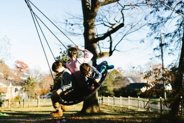 Cousins on swing under trees in front yard in neighborhood clipart