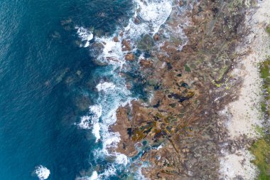 overhead drone view of waves splashing in a rocky shore clipart