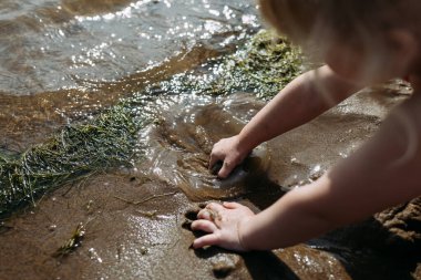 Küçük çocuk göl kıyısında kum ve suyla oynuyor.