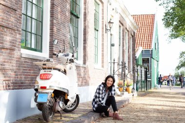Amsterdam 'da kaldırımda motosikletin yanında oturan kadın.