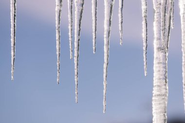 Buz saçaklarının yakın çekimi açık bir kış gökyüzüne karşı asılı.