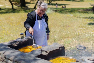 Beyaz önlüklü bir kadın tipik bir İspanyol paella pişiriyor.