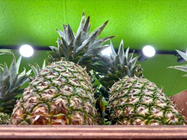 Close-up of pineapples on shelf under bright lights in NYC market clipart