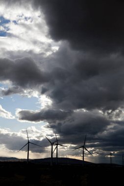 Rüzgar türbinleri fırtınalı gökyüzü altında alacakaranlıkta.