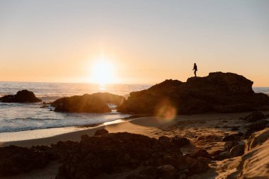 Gün batımı denizine bakan kayalıklardaki siluet.