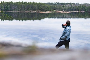 Woman Looking out at Reflective Lake Surrounded by Trees clipart