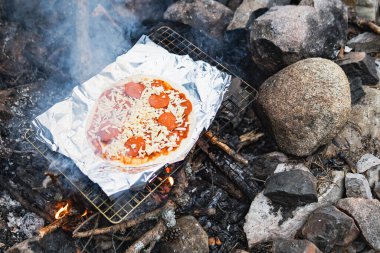 Açık hava kamp ateşinde pişen biberli ve peynirli pizza.