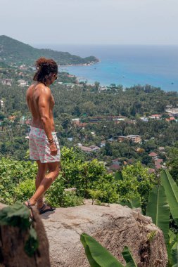 Tayland 'da bir körfeze bakan kıvırcık saçlı, gömleksiz bir adam.