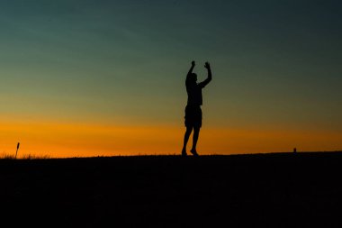 Bir insanın silueti renkli bir günbatımı gökyüzüne karşı el kaldırıyor..