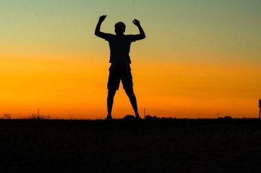 Canlı bir günbatımı gökyüzüne zıplayan bir insanın silueti..